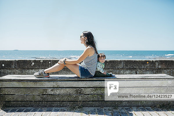 France  mother and baby girl sitting back to back on a bench at beach promenade
