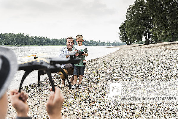 Father with two sons playing with drone at the riverside
