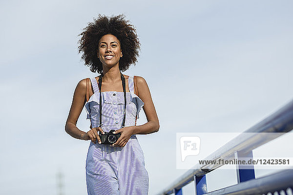 Portrait of smiling young woman with camera against sky