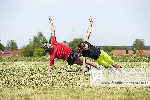 Couple doing side plank exercise on meadow