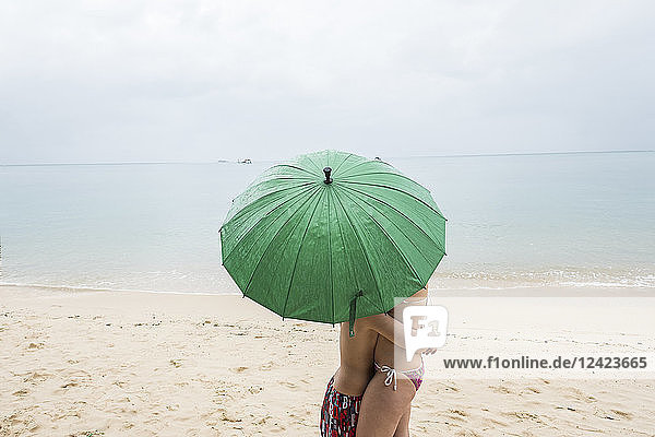 Thailand  boy hugging his mother on the beach under a green umbrella