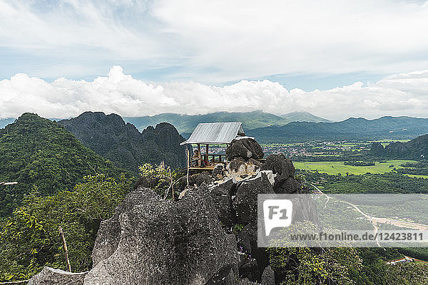 Laos  Vang Vieng  man in hut on top of rocks overlooking landscape of rice fields