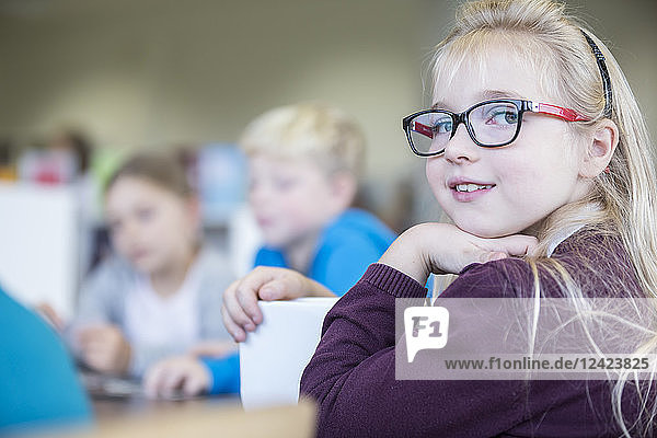 Portrait of smiling schoolgirl with classmates in class