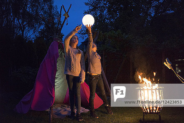 Two girls standing in front of tipi  holding lamp as moon