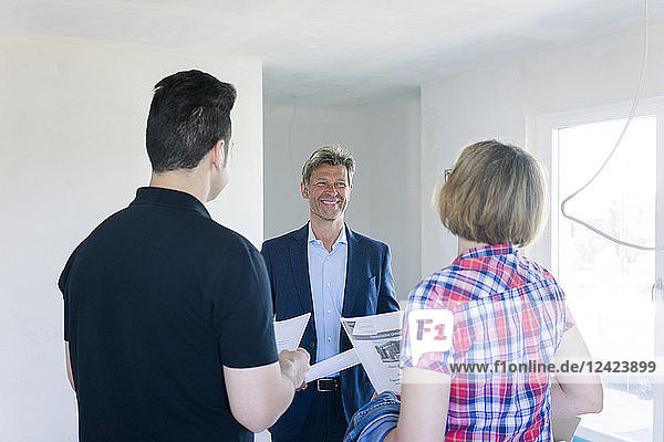 Smiling man in suit talking to couple in unfinished building