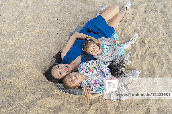 Happy mother with two daughters lying on the beach