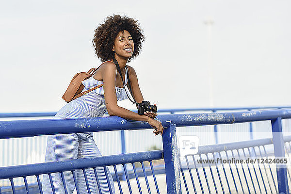 Portrait of fashionable young woman with backpack and camera on a bridge