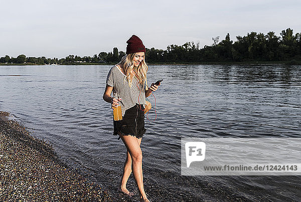 Young woman walking barefoot on riverside  earphones and smartphone