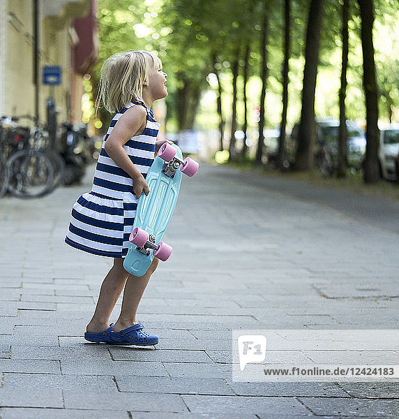 Happy little girl with skateboard on pavement