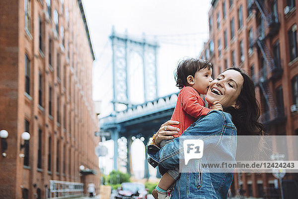 USA  New York  New York City  Baby kissing mother in Brooklyn with Manhattan Bridge in the background