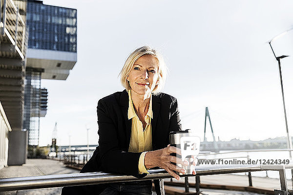 Smiling senior businesswoman with takeaway coffee at the riverside