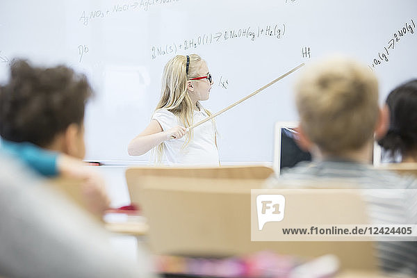 Schoolgirl explaining formula at whiteboard in class