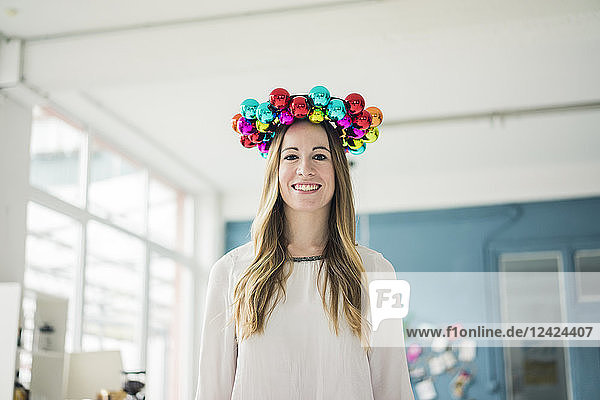 Portrait of smiling woman with colourful Christmas bauble wreath on her head