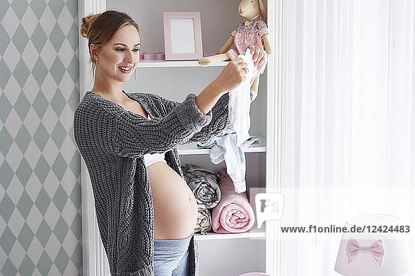 Pregnant woman with baby clothes in baby room