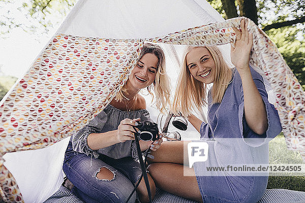 Two happy young women with old-fashioned camera in a teepee in a park