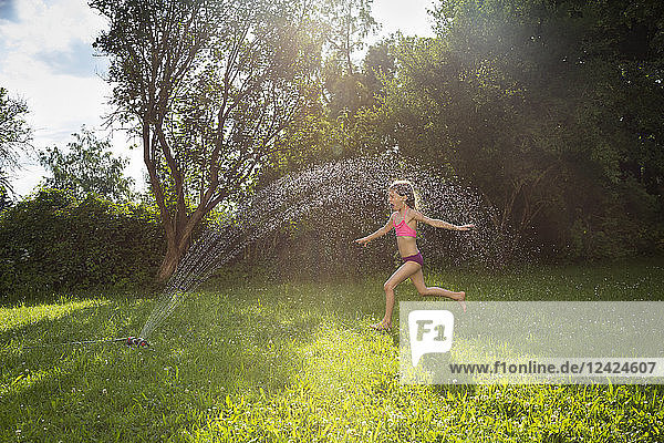 Little girl having fun with lawn sprinkler in the garden
