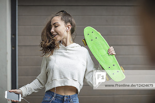 Carefree teenage girl dancing while holding skateboard and listening to music