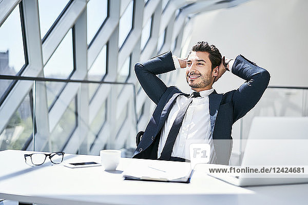 Smiling businessman leaning back at desk in modern office