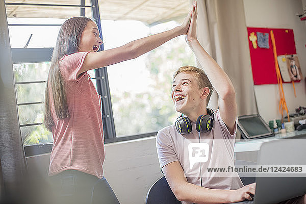 Happy teenage girl and boy with laptop high fiving