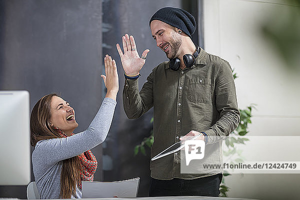 Two colleagues giving a high five at desk in office