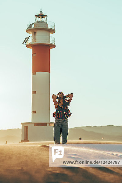 Young woman with windswept hair standing in desert landscape at lighthouse