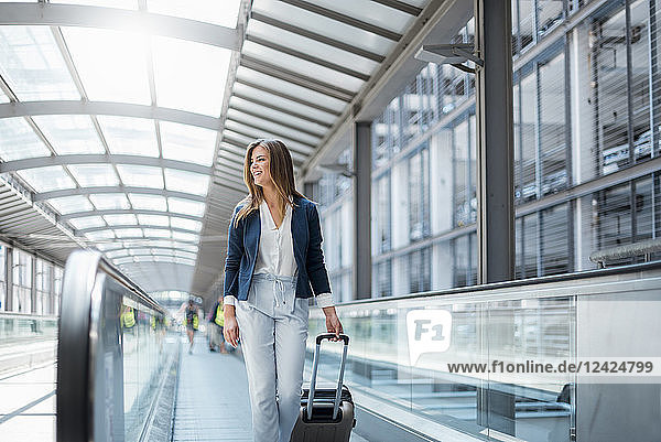 Smiling young businesswoman with baggage on moving walkway
