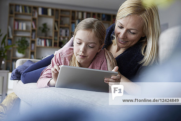 Mother and daughter lying on couch  using digital tablet