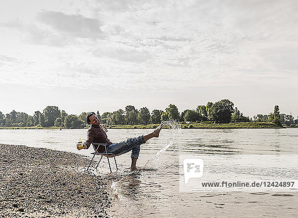 Mature man sitting on chair at Rhine riverbank