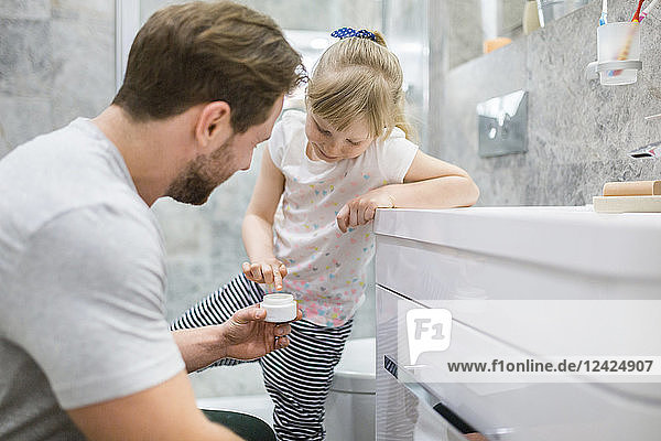 Father and daughter using face cream in bathroom