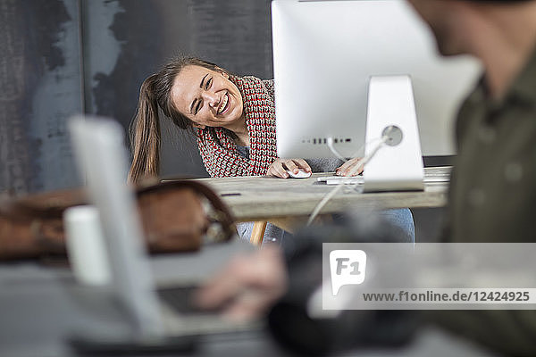 Happy young woman peeking around computer screen in office