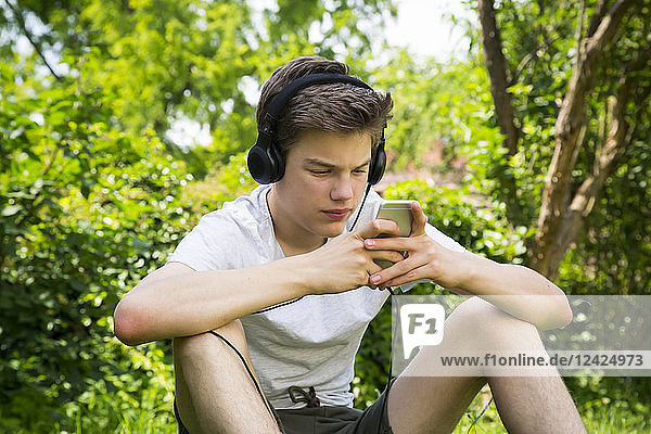Boy sitting in the garden listening music with headphones and smartphone