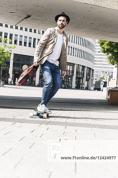 Young man with guitar riding skateboard in the city