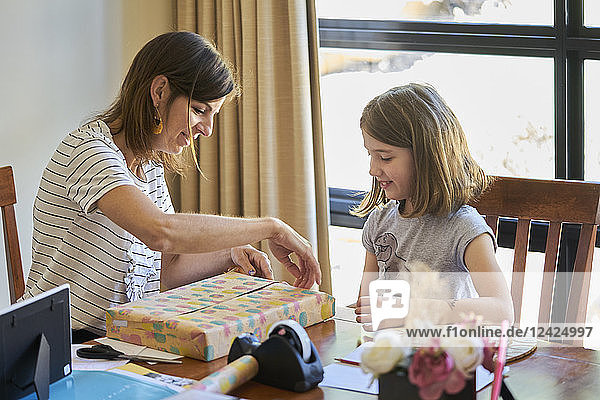 Mother and daughter packing gift at table at home