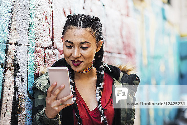 Portugal  Lisbon  Smiling young woman looking at smartphone  leaning against wall