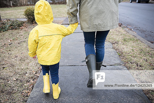 Mutter und Tochter (2-3) halten sich an den Händen und gehen an einem regnerischen Tag spazieren