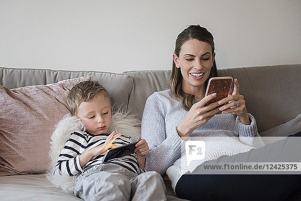 Mutter und Sohn (4-5) sitzen auf dem Sofa mit Smartphones in den Händen