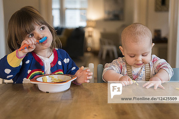 Sisters (12-17 months  2-3) having lunch at home