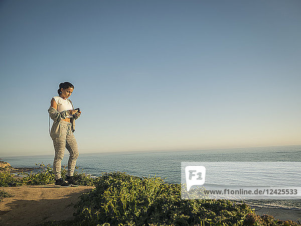 USA  Kalifornien  Newport Beach  Frau steht auf Klippe und schaut auf Telefon