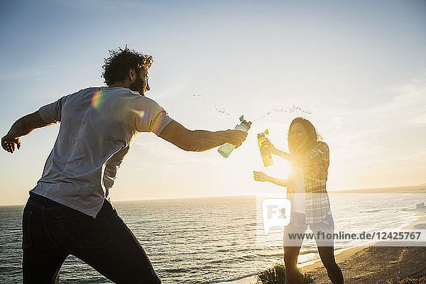 Couple having water fight on beach at sunset
