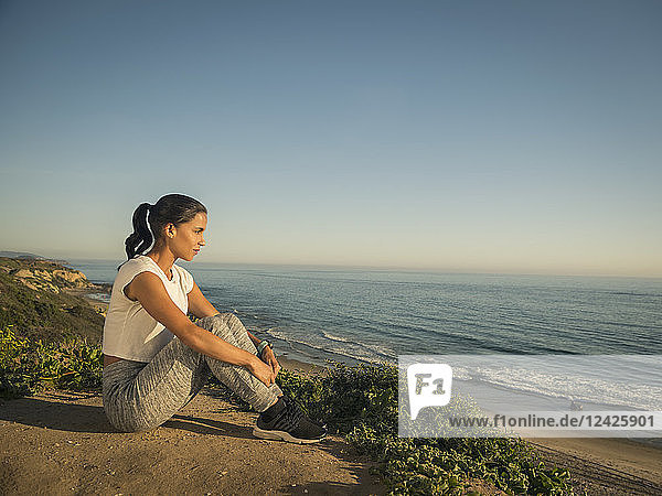 USA  California  Newport Beach  Woman in sport suit sitting on cliff and looking at view