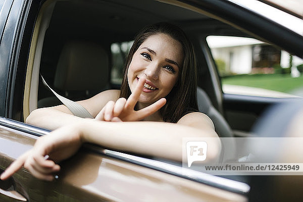 Lächelnde junge Frau macht Friedenszeichen im Auto