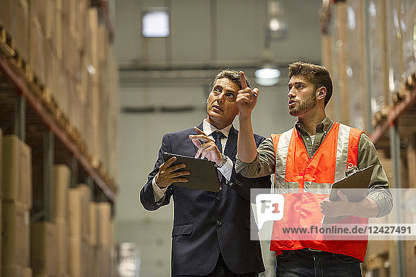 Worker and businessman with digital tablet and clipboard in warehouse