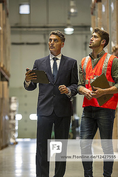 Arbeiter und Geschäftsmann mit digitalem Tablet und Klemmbrett im Lager