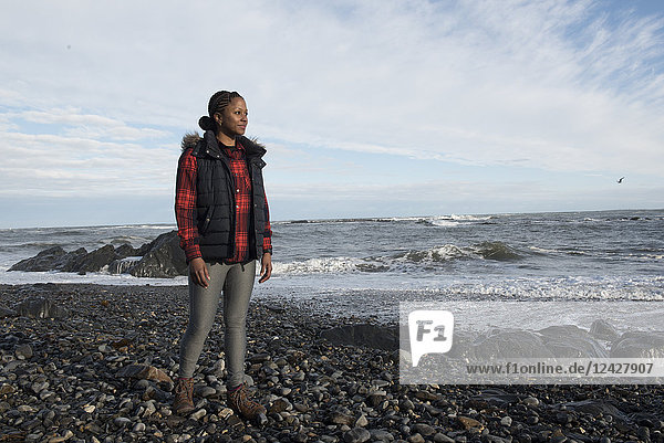 Full length portrait of smiling African American woman standing on gravel beach against sea