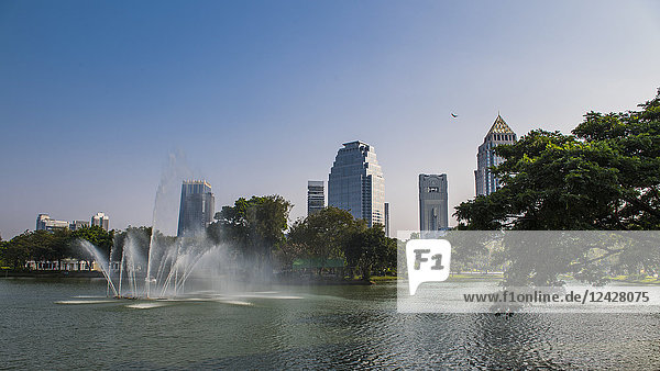 View of fountain in lake at Lumphini Park under clear sky and skyline of city of Bangkok  Thailand