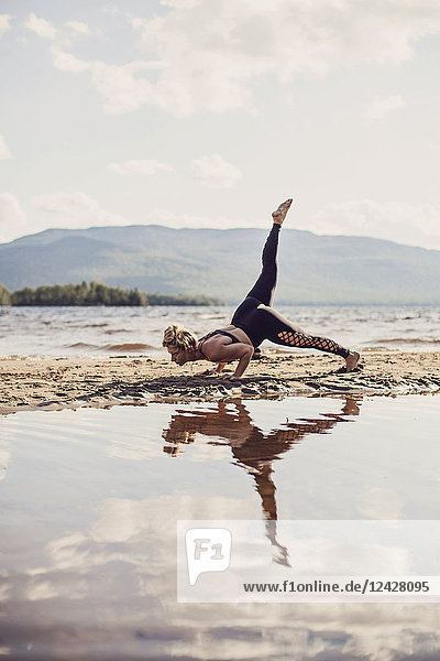 Eine fitte junge Frau praktiziert Yoga an einem Strand am Flagstaff Lake in Maine.