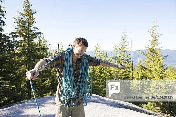 Taillenaufnahme eines einzelnen männlichen Bergsteigers  der ein Seil in einer natürlichen Umgebung aufwickelt