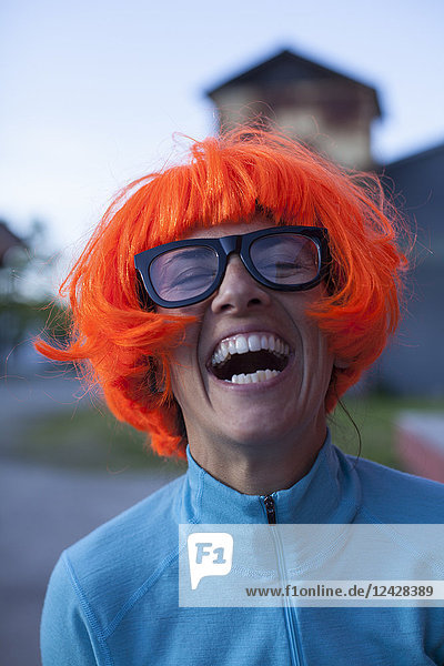 Humorvolles Porträt einer Frau mit orangefarbener Perücke und Brille  die lacht