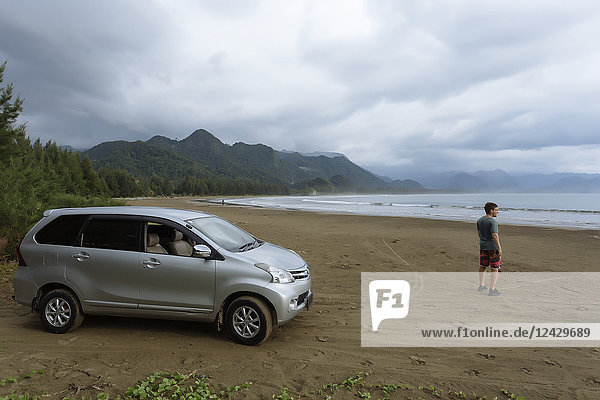 Young man with car on sandy beach under overcast sky  Banda Aceh  Sumatra  Indonesia
