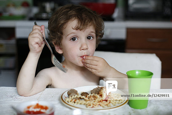 Little boy eating spaghetti at table at home